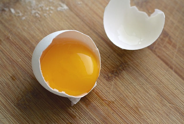 Half-cracked egg with yolk on a wooden surface