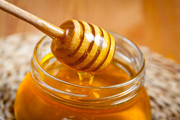 Wooden honey dipper in a jar of honey with a blurred background